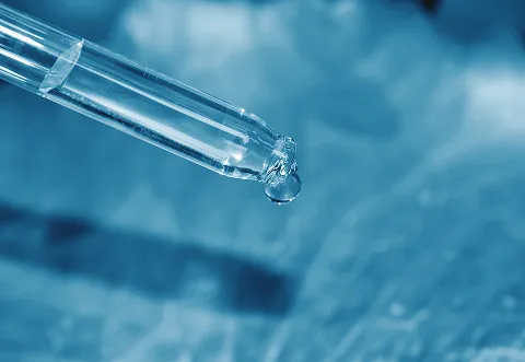 Close-up of a glass dropper releasing a single drop of liquid, with a blue-toned background.